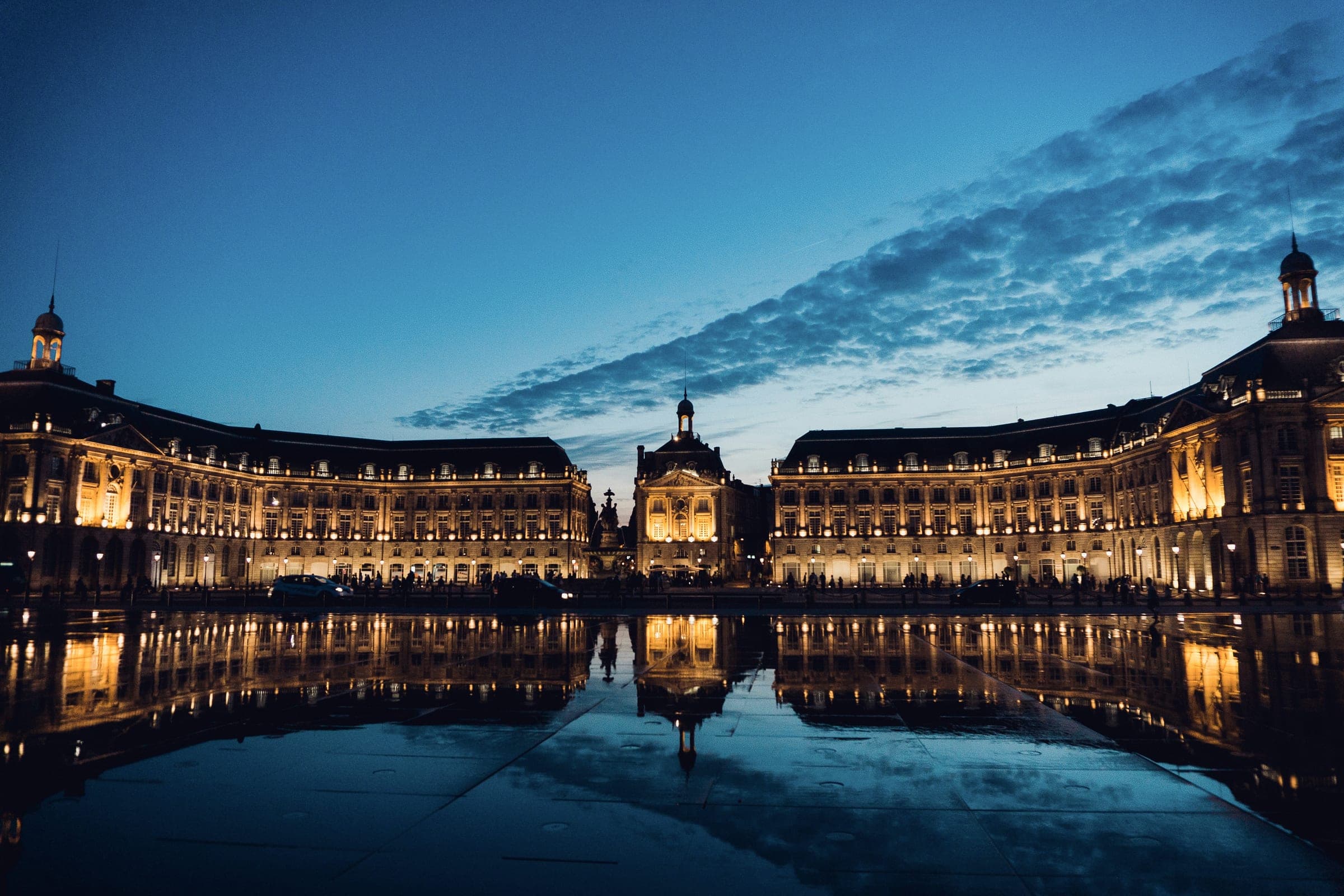 Grande place classique illuminée à la tombée de la nuit, reflétée dans un miroir d'eau